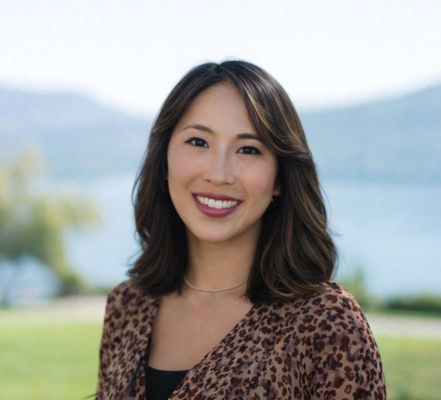 Smiling Asian woman with dark hair in a leopard print top, outdoors with a blurred lake and hills in the background.