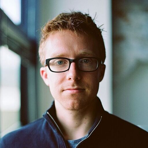 a man wearing glasses and a blue jacket is looking at the camera .