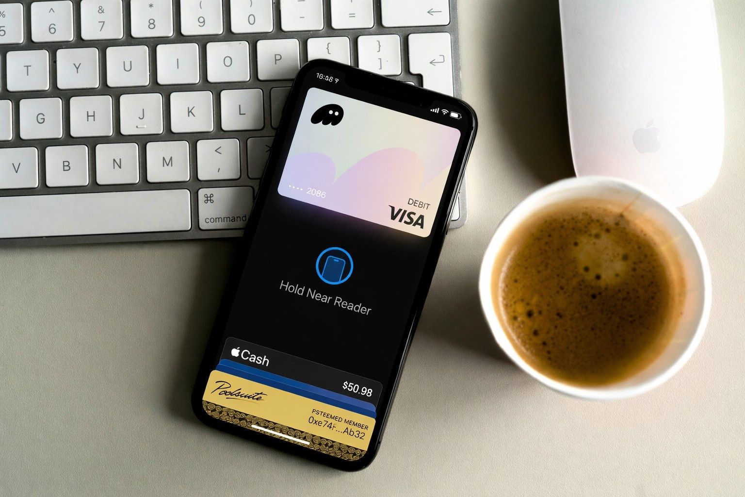 An iPhone displaying a Phantom Debit card in Apple Pay, alongside a keyboard, mouse, and coffee.