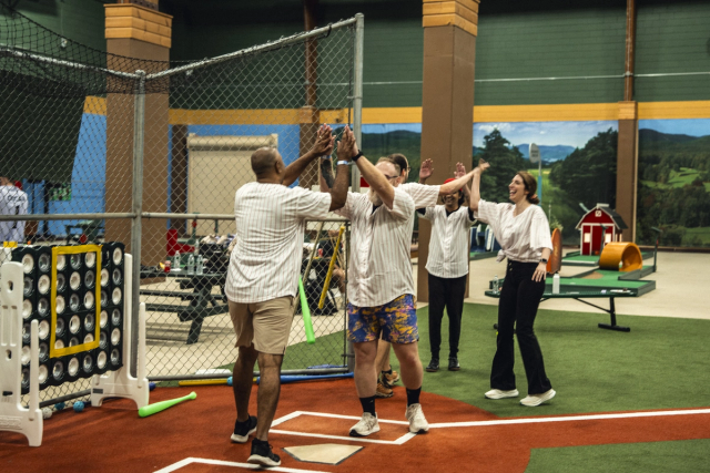 Adults high-fiving and celebrating on an indoor baseball field.