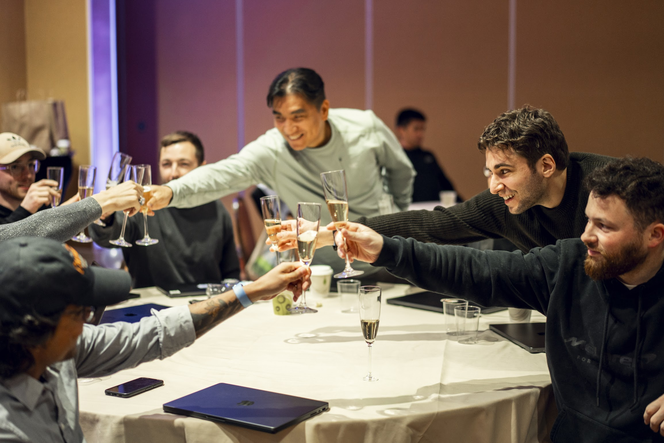 A group of people raising champagne flutes in a toast around a table.